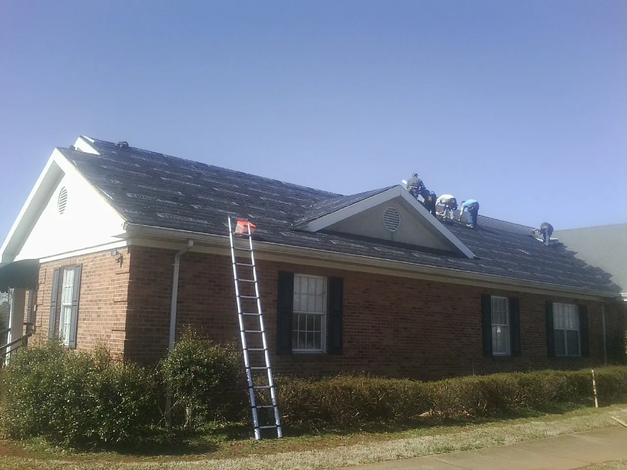 Crew tearing shingles off a brick ranch roof with a ladder set — Emergency Roof Repair work by our crew in Dittmer
