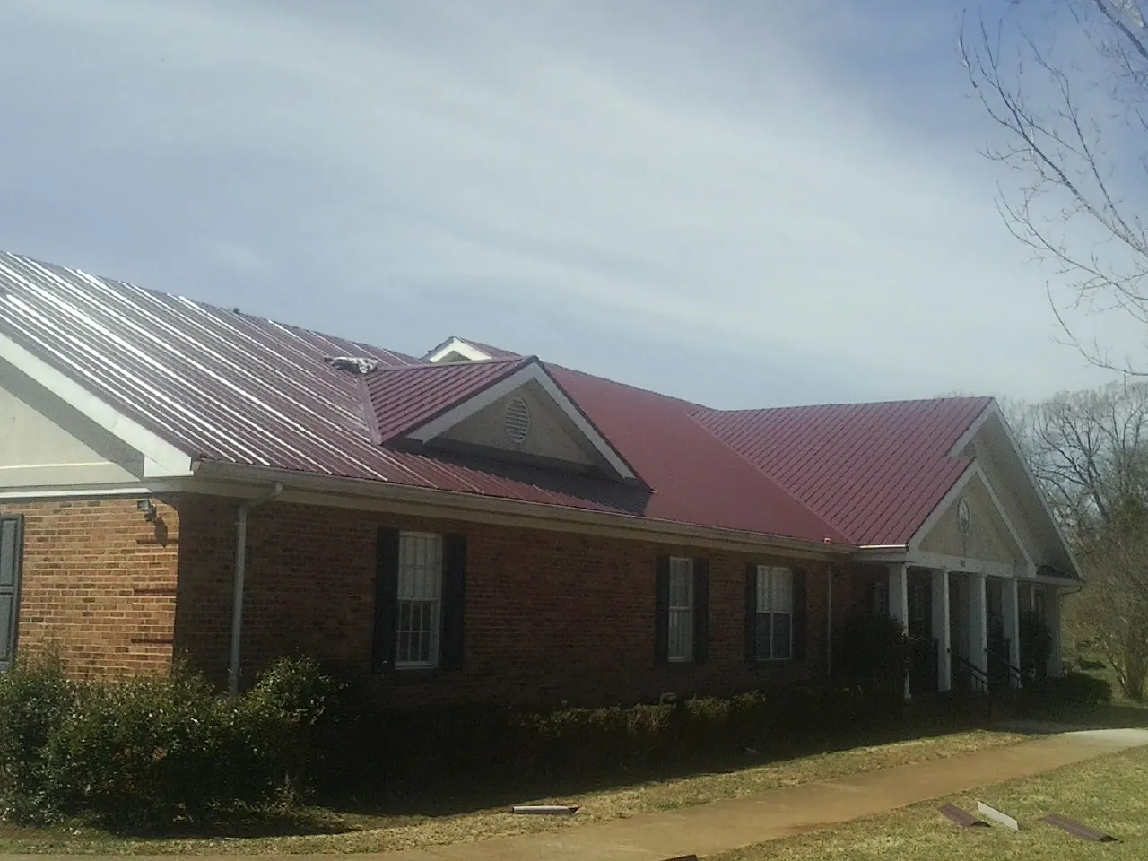Red metal roof with gabled entries on a long brick building, from a Hail Damage Roof Repair job in Dittmer