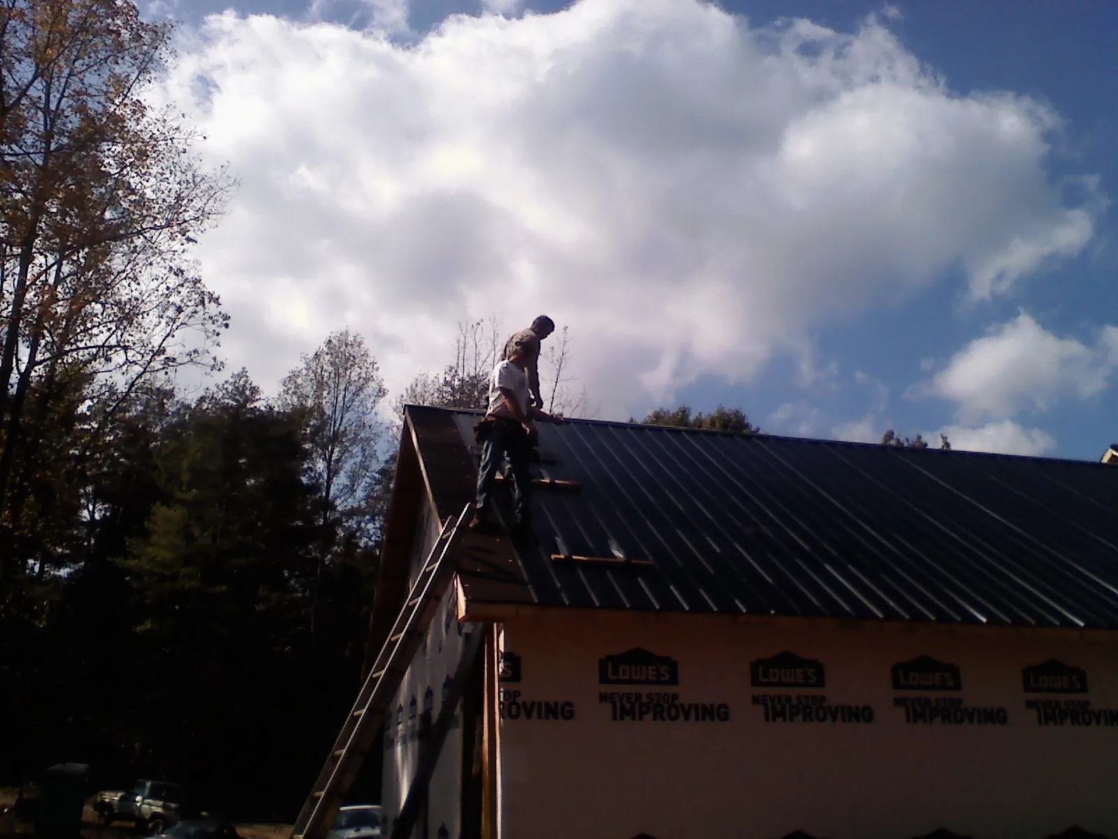 Roofer fastening dark metal panels high against a cloudy sky, from a Roof Inspection job in Dittmer